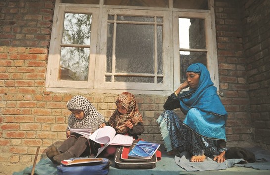 A woman looks on as her daughters study outside their house on the outskirts of Srinagar yesterday.