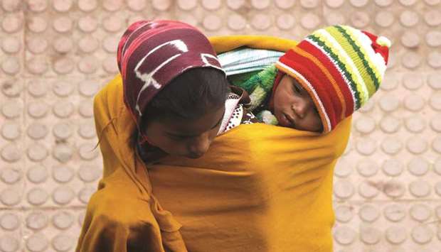 A woman wraps a child in a shawl while waiting for a train at a railway station on a foggy winter morning on the outskirts of Agartala, yesterday.