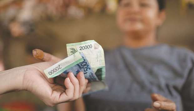 A customer hands Indonesian rupiah banknotes to a vendor at a market in Jakarta (file). With Muslims making up almost 90% of Indonesiau2019s 265mn population, policymakers are trying to make up for the lost time in tapping the global halal economy that has tripled to $6.4tn from 2012.