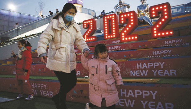 A woman wearing a face mask, following the Covid-19 outbreak, walks with a child past a 2022 installation on New Yearu2019s Eve at a shopping mall in Beijing.