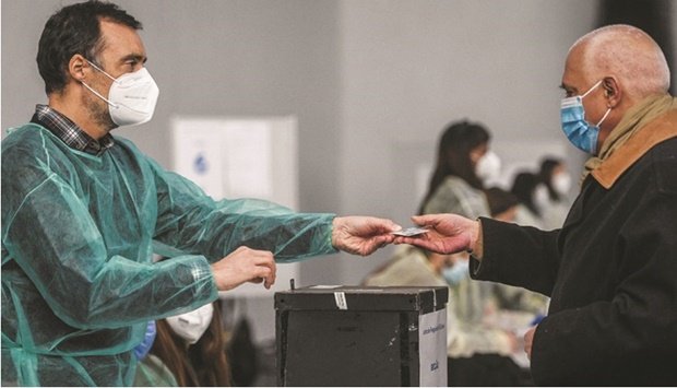 An official wearing a protective suit checks the documents of a voter casting his vote at the Estrela polling station in Lisbon yesterday. (AFP)