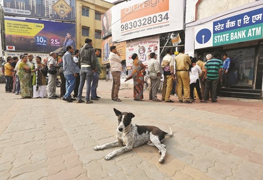 A stray dog rests as people queue outside an ATM to withdraw cash in Kolkata