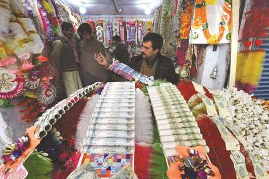 A shopkeeper makes garlands with US dollars and local currency notes at a flower market in Peshawar. Garlands made up of currency notes is popular in south Asia for special occasions like weddings, pilgrimage, and political activities.