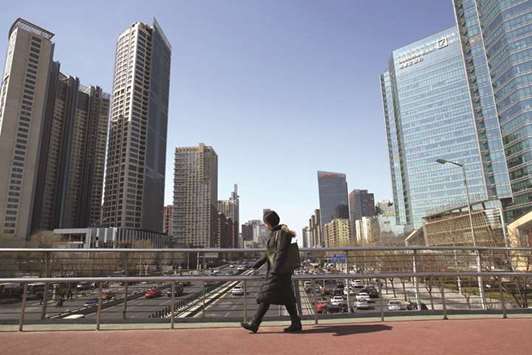 A woman crosses a footbridge in front of towers at Kaisa Plaza,  developed by Kaisa Group Holdings (left) in Beijing. Kaisa Group, which defaulted on notes in 2015, sold in excess of $5bn of bonds, according to data compiled by Bloomberg.