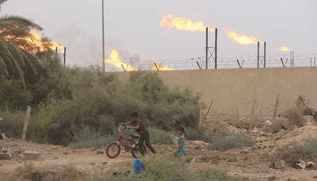 Children play in their homeu2019s backyard as flames rise from oil refinery pipes in the background in Basra (file). Iraq is Opecu2019s biggest producer after Saudi Arabia.