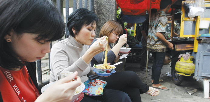 Women eat noodles purchased from a street food stall in Jakarta.