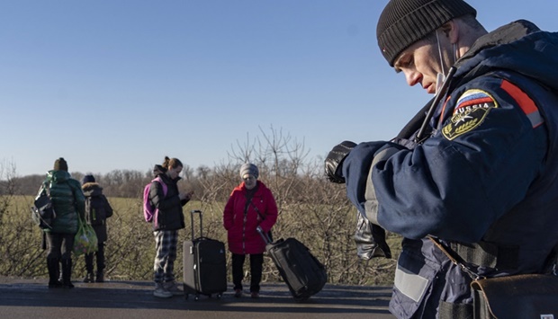 People carry their belongings as they cross the Russian border check point as a rescuer of the Russian Emergency Ministry looks on near the town of Uspenka, on February 19, 2022.