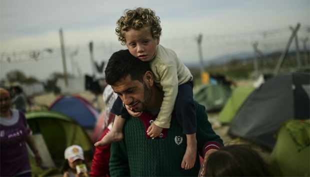 A man carries a child as migrants and refugees carry on with their daily lives at the makeshift camp along the Greek-Macedonian border, near the Greek village of Idomeni. AFP