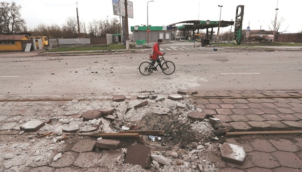 A resident walks with a bicycle along a street, which has been damaged due to the ongoing conflict with Russia, near the Illich Steel and Iron Works factory, in the southern Ukraine port city of Mariupol.