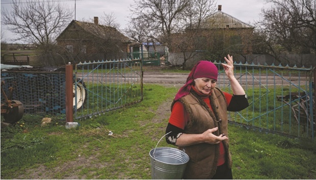 Olga Tus gestures as she stands in front of a house damaged by a rocket attack as she makes her way to milk her cow amid the sound of regular nearby shelling in the village of Mala Tokmatchka. (AFP)