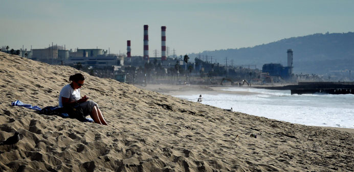 A woman sits on a sand berm created by city workers to protect houses from El Nino storms and high tides at Playa Del Rey beach in Los Angeles on Mond