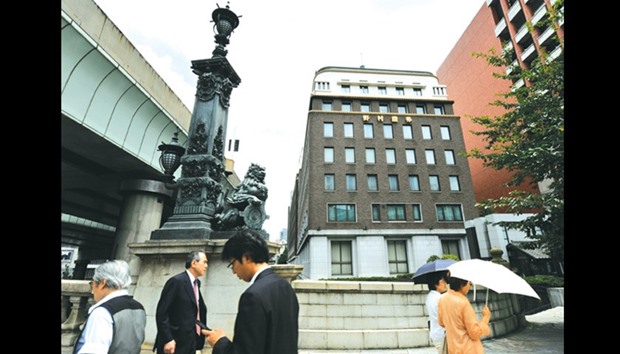 Pedestrians walk past the headquarters of Nomura Holdings. Nomura is in discussions to sell its stake of about one-third in the brokerageu2019s real estate unit to Japan Post Holdings.