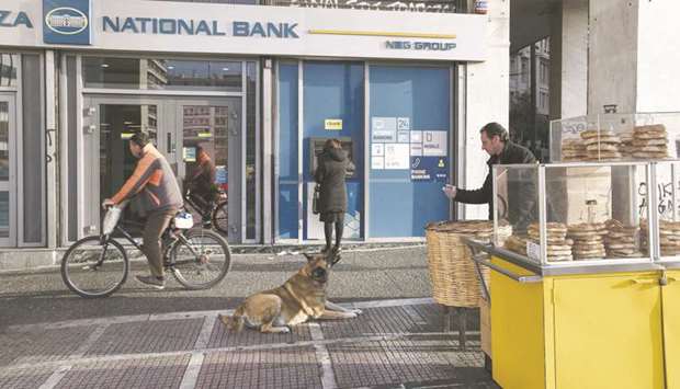 A street vendor feeds a stray dog outside a National Bank of Greece bank branch in Athens. Greek lenders, still struggling with the aftermath of the 2012 sovereign debt crisis, risk being moved back to square one as the coronavirus complicates the countryu2019s ambitious plan to pare back its bad loans.