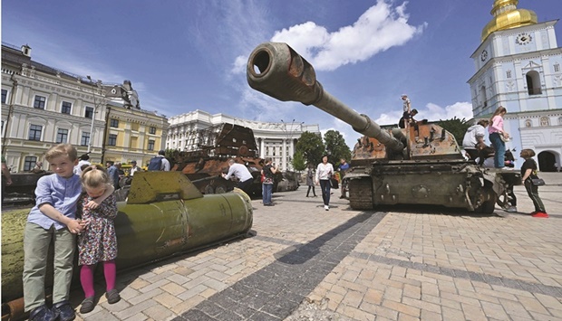 Two children sit on a fragment of Russian rocket Tochka-U past a damaged tank at open air exposition of destroyed Russian equipment in the centre of Kyiv yesterday. (AFP)