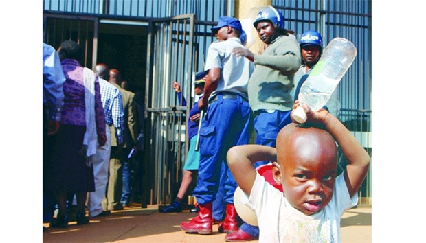 A boy stands in front of anti-riot police at the entrance at the Harare Magistratesu2019 court, where veteransu2019 body spokesman Mahiya was charged with insulting Mugabe.