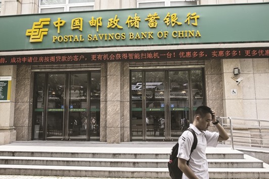 A pedestrian walks past a Postal Savings Bank of China branch in Shanghai. The bank, Chinau2019s sixth largest in terms of assets, is seeking to raise $8bn in what could be the worldu2019s largest IPO this year, according to people familiar with the matter.