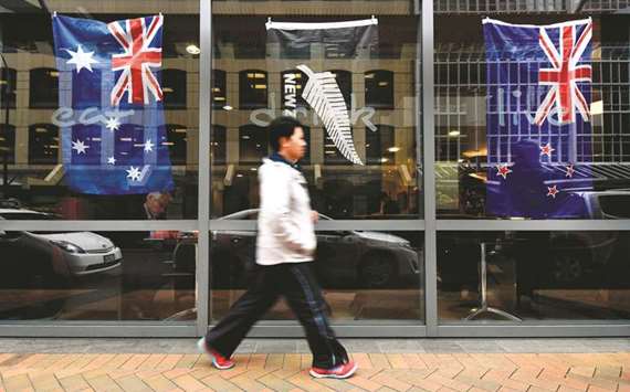 A man walking past a window displaying New Zealandu2019s national flag (right) and Australiau2019s national flag in Wellington.