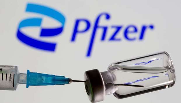 Syringe and vial are seen in front of displayed new Pfizer logo