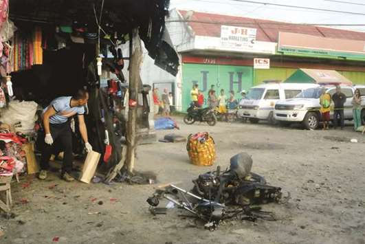 A police investigator (left) gathers evidence at the site of a bomb blast in Isulan town on the southern island of Mindanao, yesterday.