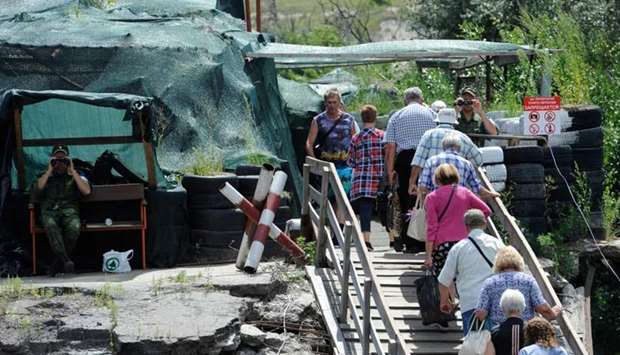 Russia-backed separatists watch as people walk across a destroyed bridge between the Ukraine-controlled territory and territory held by Russia-backed separatists at a checkpoint near the village of Stanytsia Luhanska, in Luhansk region, eastern Ukraine on August 1