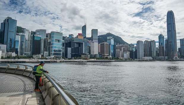 A man fishes as buildings stand across the Victoria Harbor in Hong Kong. Dividend investors are having to rethink their strategies in Hong Kongu2019s stock market, as companies mired in a pandemic-driven recession are slashing payouts more than before.