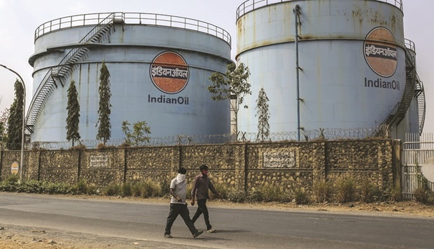 Pedestrians walk along a road past storage tanks in a Indian Oil Corp facility near Jawaharlal Nehru Port in Navi Mumbai, India. The three biggest state-run retailers, which together supply more than 90% of Indiau2019s petroleum fuels, have suffered the worst quarterly losses in years by absorbing record international crude prices.