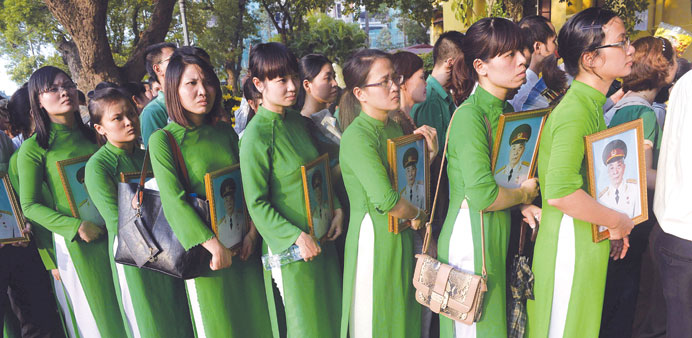 Women in traditional dress holding framed portraits of the late General Vo Nguyen Giap as they line up to pay final respects to him at his residence i